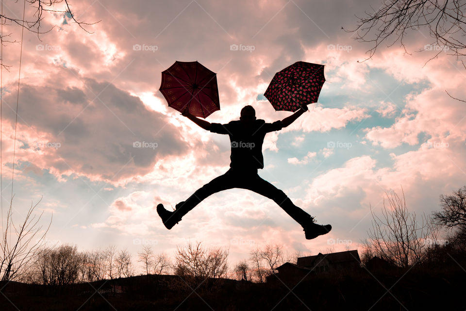 Silhouette of a man jumping holding umbrella