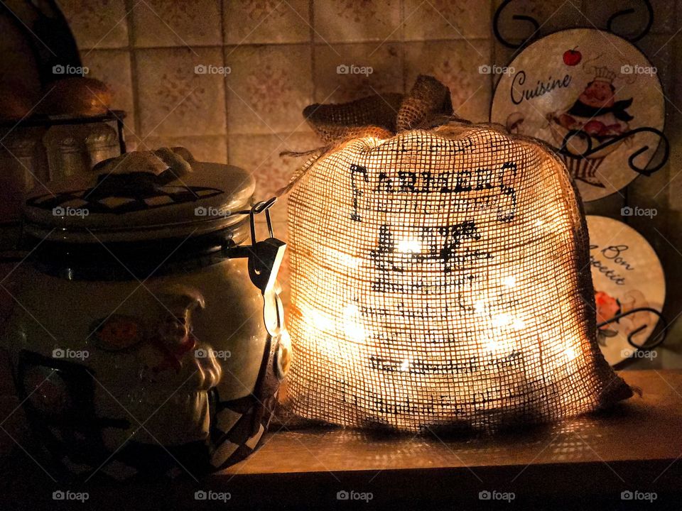 This picture is of a lot up sack surrounded by a cookie jar. They have a kitchen chef on the cookie jar and there are tiny plates behind the sack that also have a kitchen chef on them. There are lots of shadows in this picture. It looks nice how the sack is glowing. There is also salt and pepper in the background