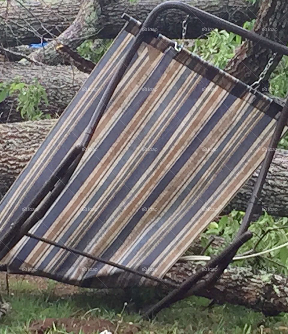 A blue gold and white striped fabric and metal hammock once used and enjoyed in our back yard made imperfect by a tornado causing a tree to fall on it.