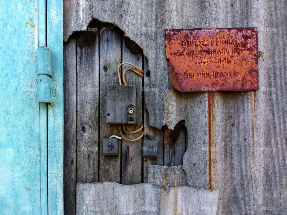 background wall with broken slate and old boards. old wiring sticks out of the wall, several switches and a meter. old rusty inscription on the plate.