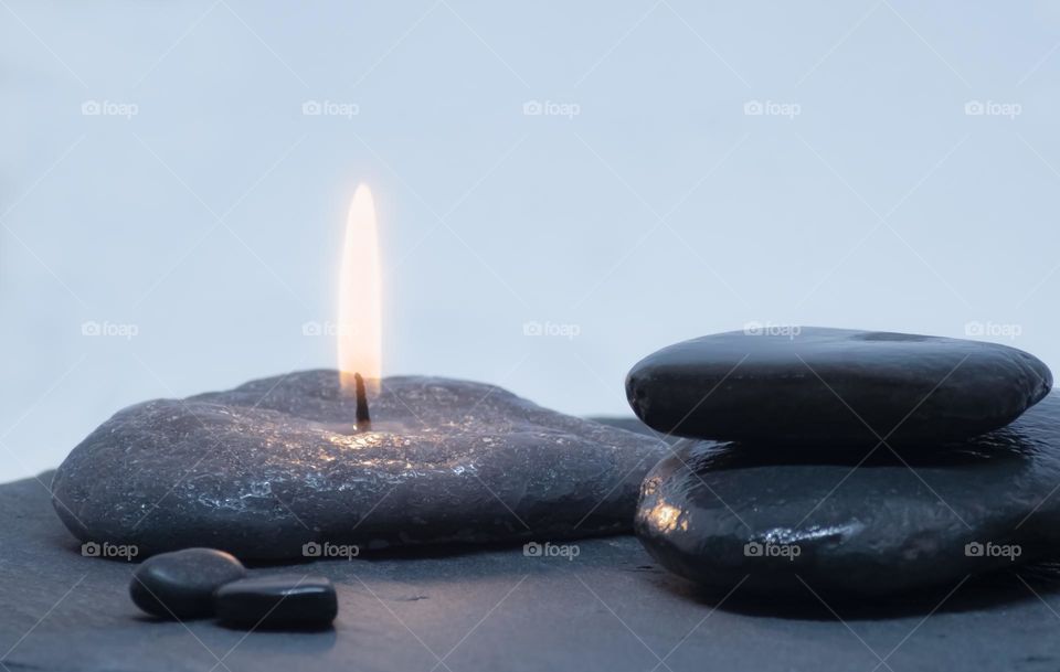 Dark river pebbles and a pebble shaped candle on a blue/grey background 