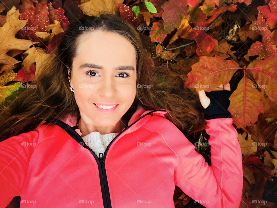 Portrait of young smiling woman surrounded by red and orange autumn leaves