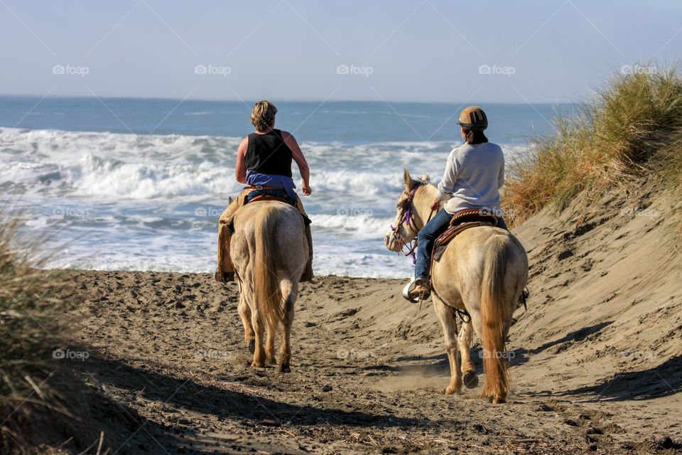 Two woman on horseback set out to explore the beach on a nice day