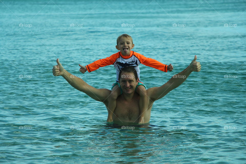 child on the shoulders of his father in the sea