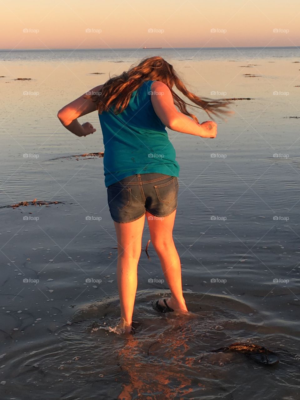 Back view young girl with long hair in shallow water at low tide 