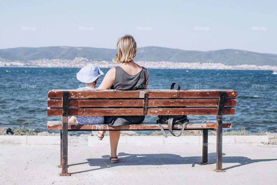 mother and daughter are sitting on the beach on a bench