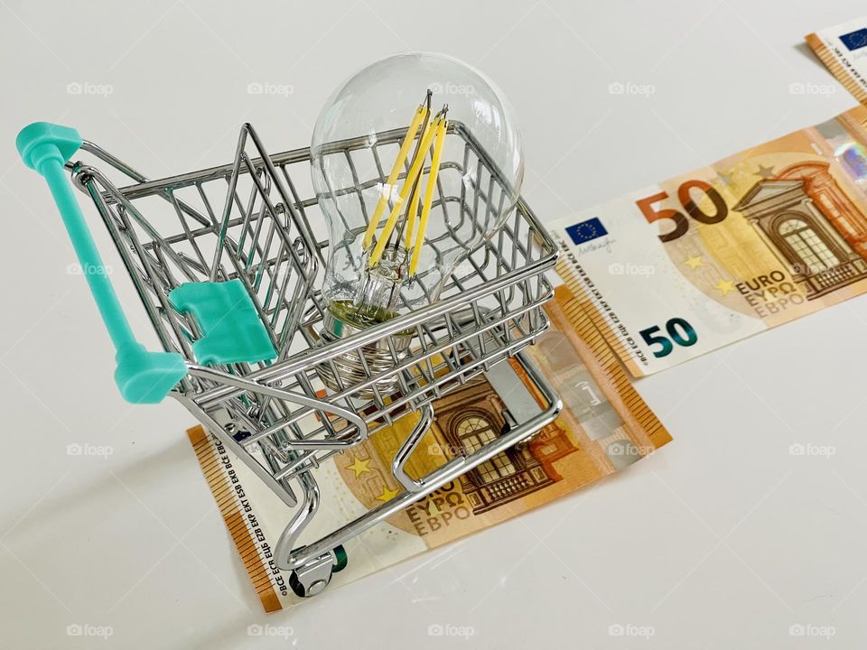 Light bulb inside a supermarket shopping trolley caddie along a path made of euro banknotes representing the increase of electricity price in Europe