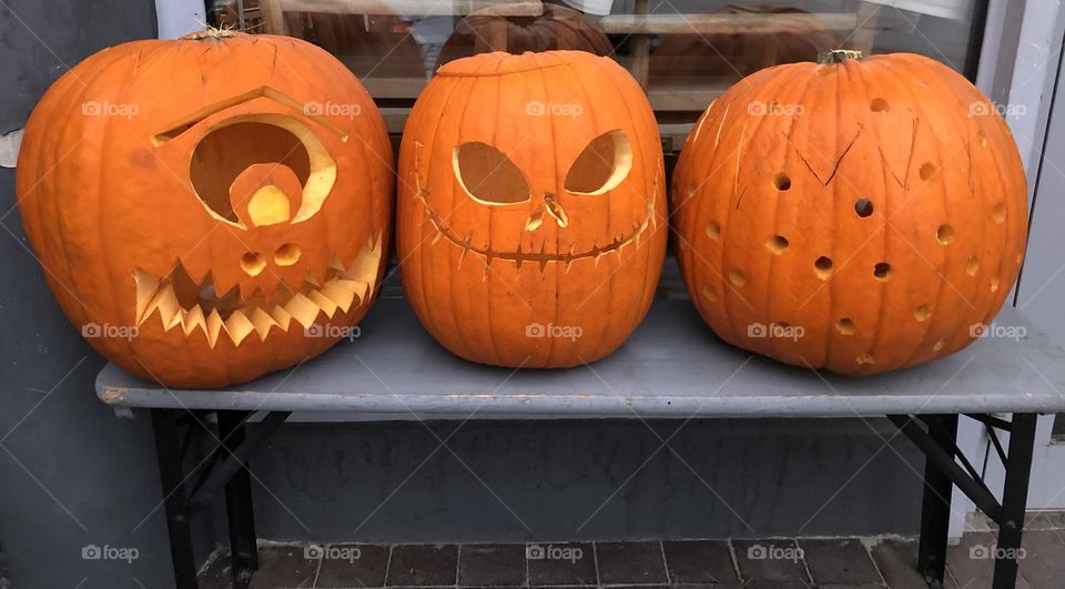 Row of three orange carved pumpkins standing outside on a bench.
