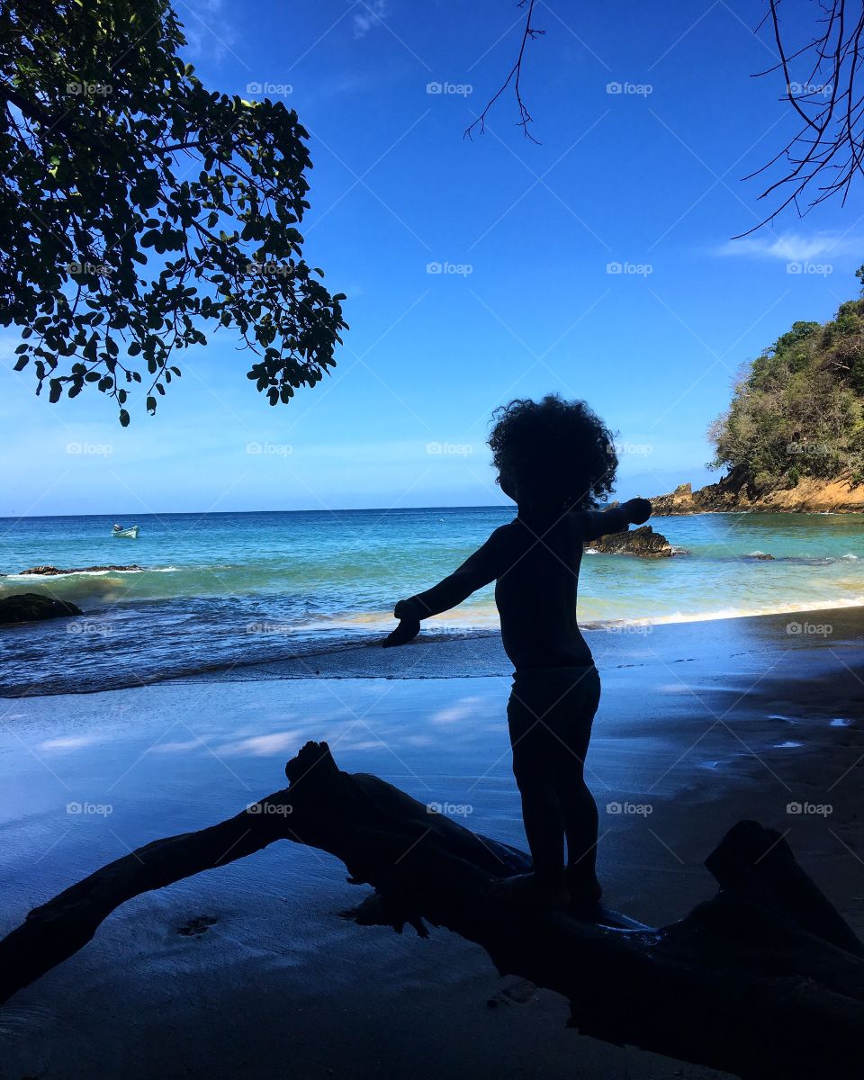 Silhouette of a child standing on driftwood at beach