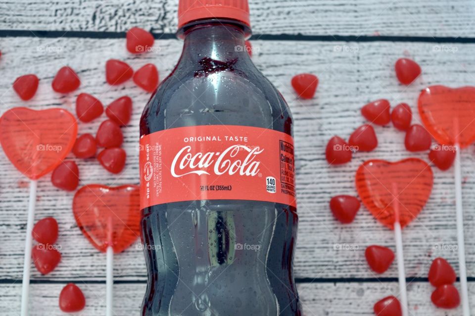 A plastic bottle of Coca-Cola with candy hearts and a white rustic background