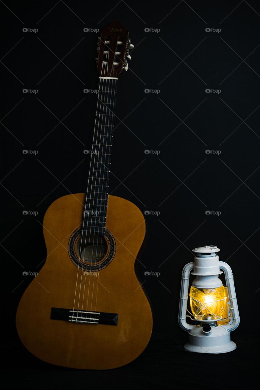 Wooden guitar next to a metal lamp, with a black background