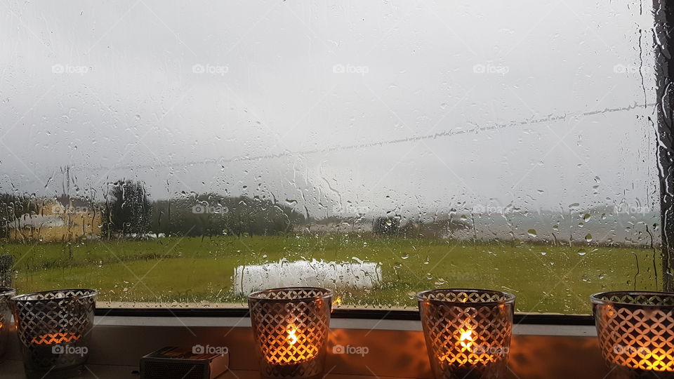 Lighted candles near a window through which we see the rain. Norway.