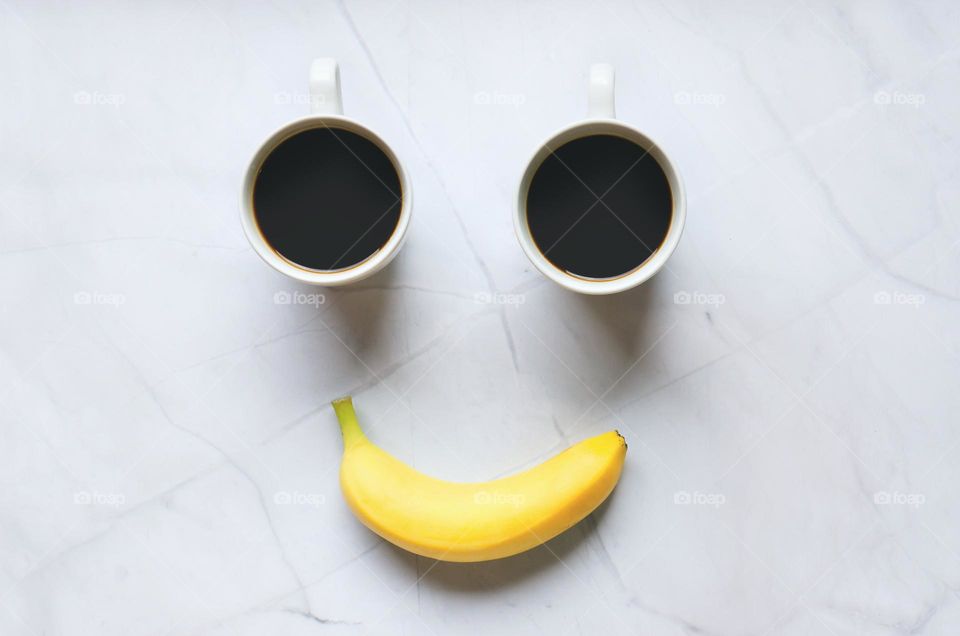 Top view of two cups of hot black coffee and yellow banana
