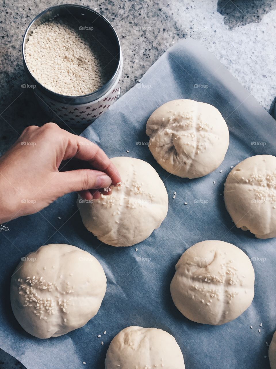 Person's hand adding sesame seeds on dough