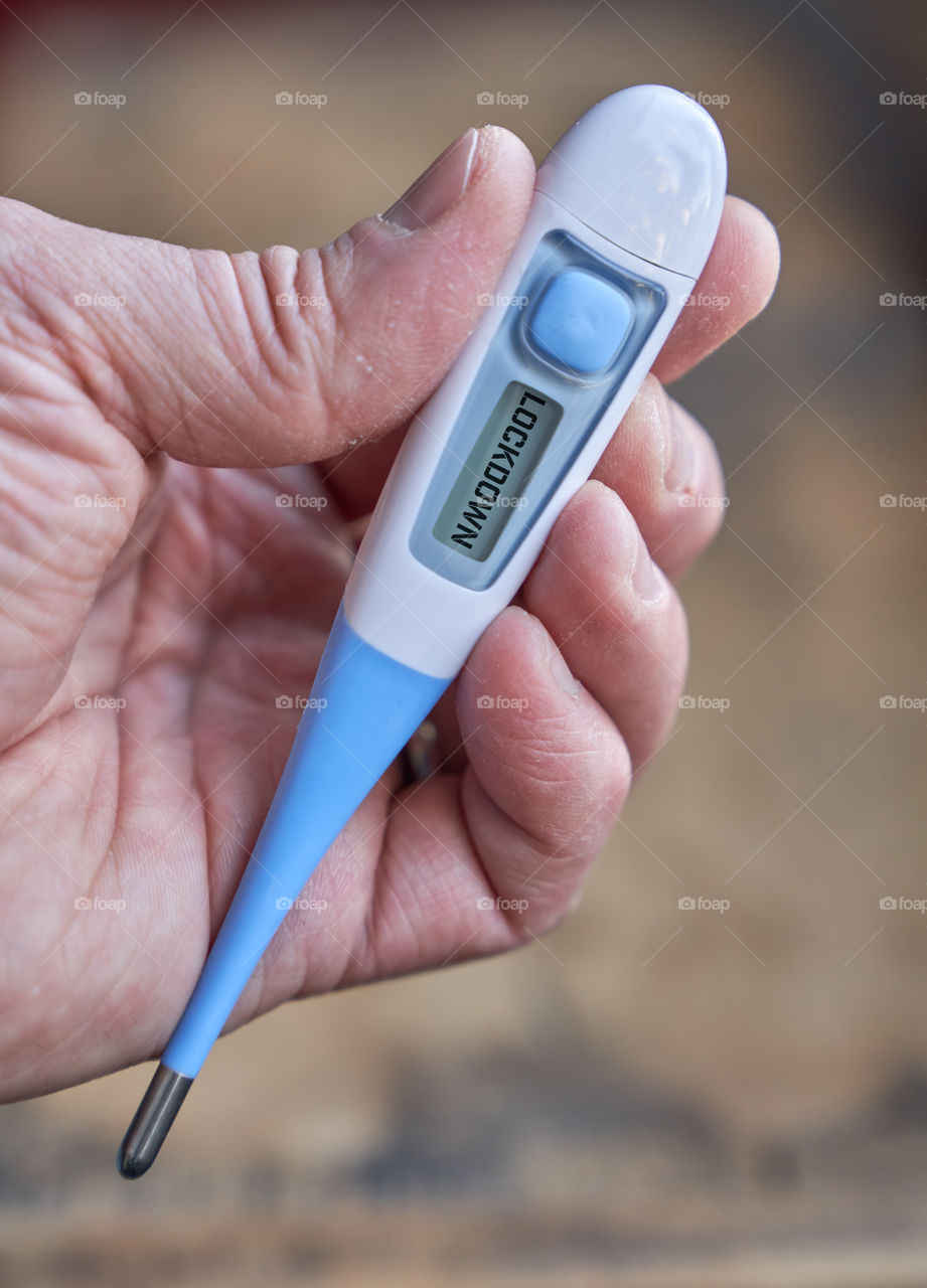 Male hand holds clinical thermometer with covid-19 text on the screen during global covid-19 or corona pandemic.