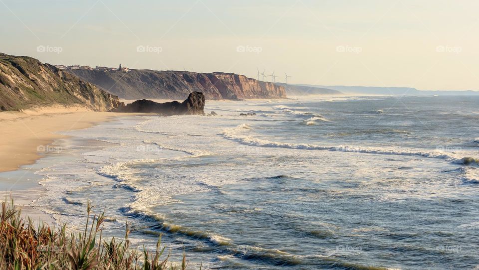 Waves roll on to the long stretch of beach at Praia da Polvoeira, with the rock formation known as Castelo/Leão reaching out into the sea