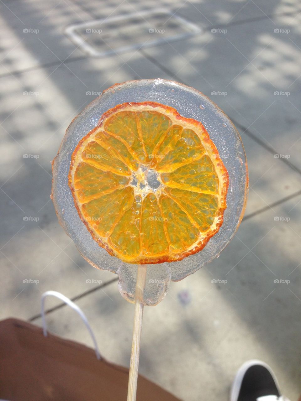 Bright orange slice in a clear lollipop with a nice one color background. Stands out on a gray sidewalk. 