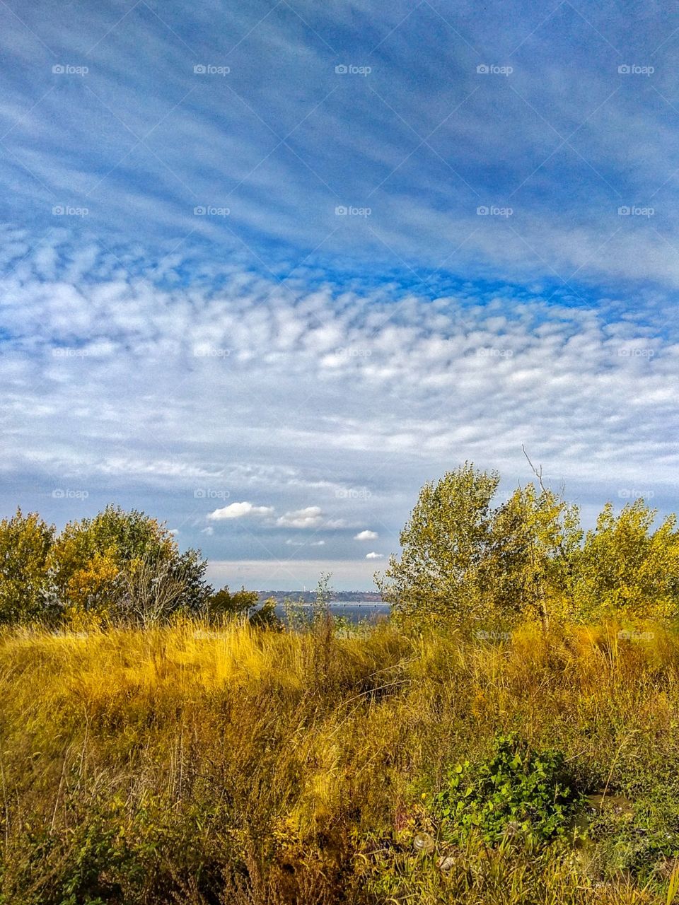 View of a very beautiful blue sky covered with a cloudy pattern, spread over the autumn landscape, above the golden grass flooded with sunlight against the background of the Volga River (Russia) and the horizon line beyond the river on a sunny day.