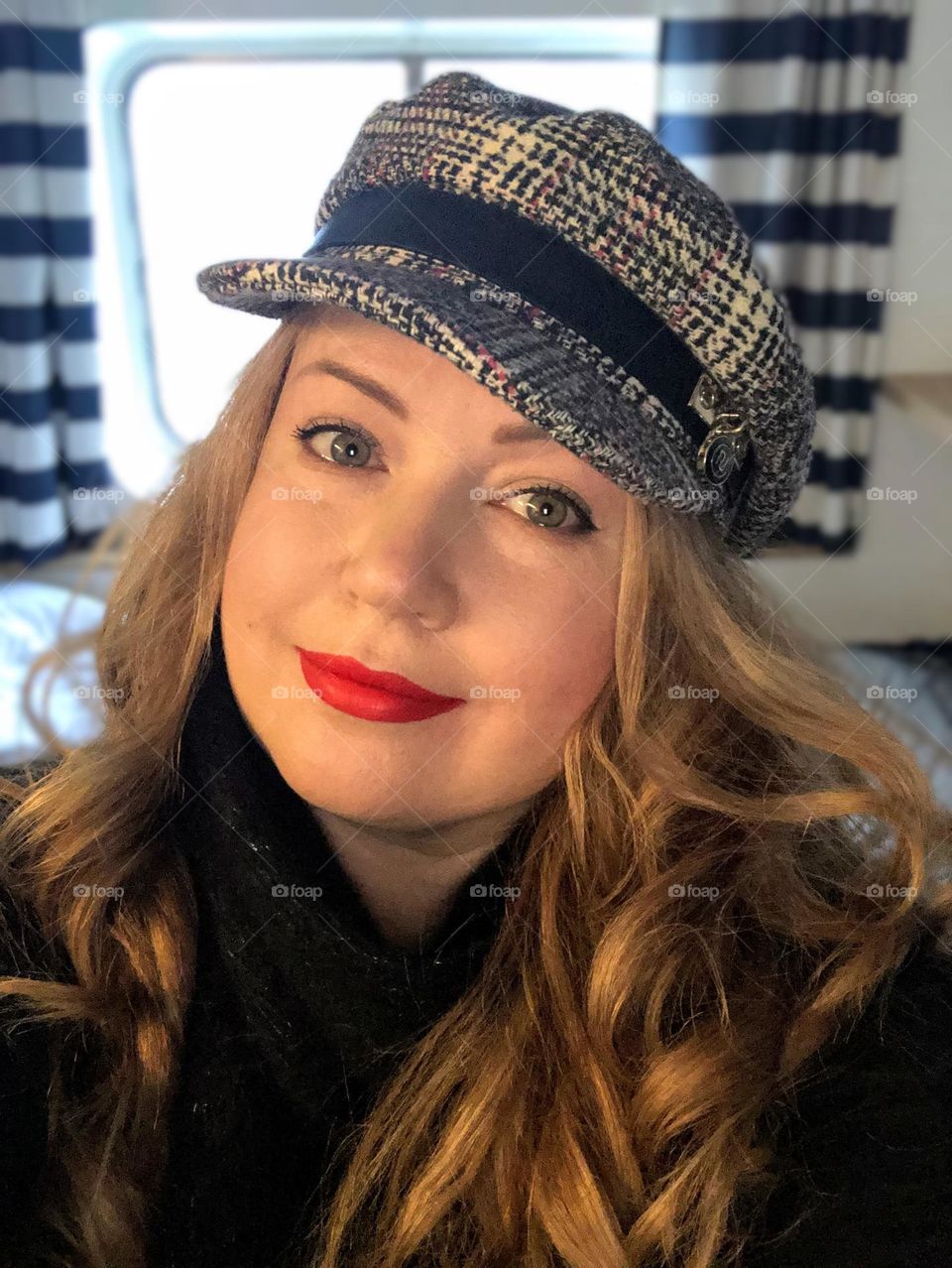 Close up portrait of happy smiling woman with the tilted head wearing cap over her long dark blond hair looking to the camera