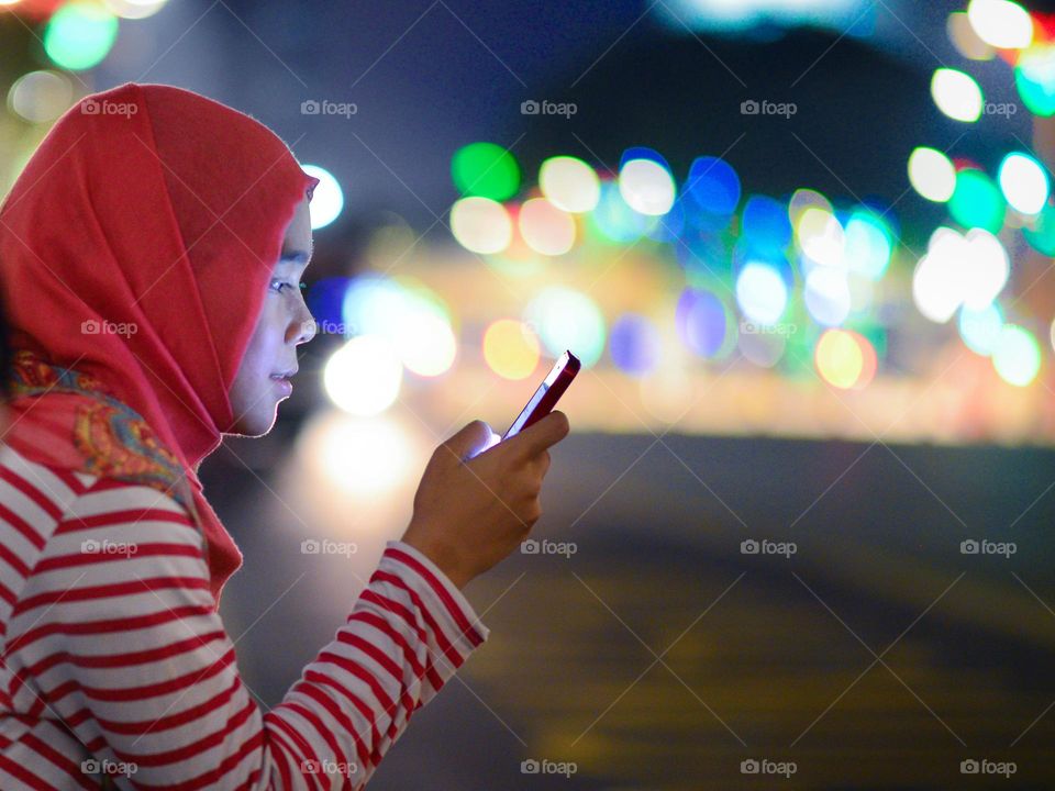 A woman in hijab texting on her phone at night in Kuala Lumpur, Malaysia