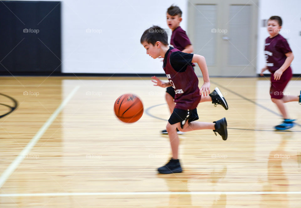 Young boy dribbling a basketball across an indoor basketball court