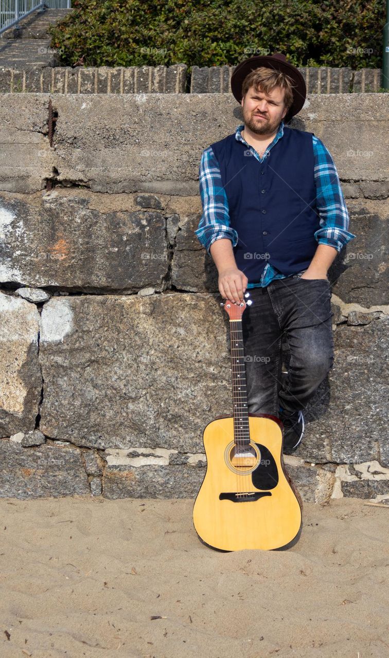 The guitarman,making some music by the docks.  He posting for a music album at the wall