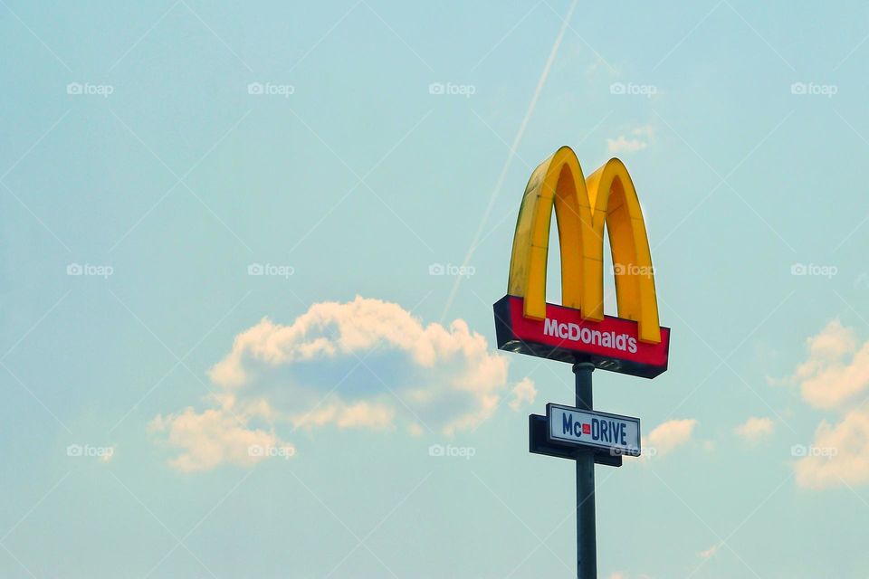 McDonald's and McDrive signage against a light blue cloudy sky