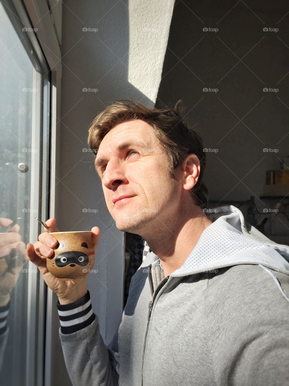 Man at window with cup of of coffee . Young Caucasian man in casual drinking hot coffee next to window