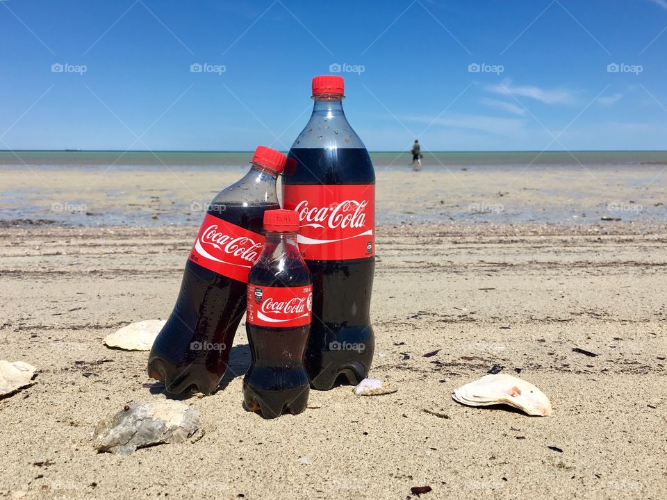 Together with Coke! Family time at the beach. Three bottles of Coca Cola conceptual family in the sand at the ocean. People in the background horizon. 