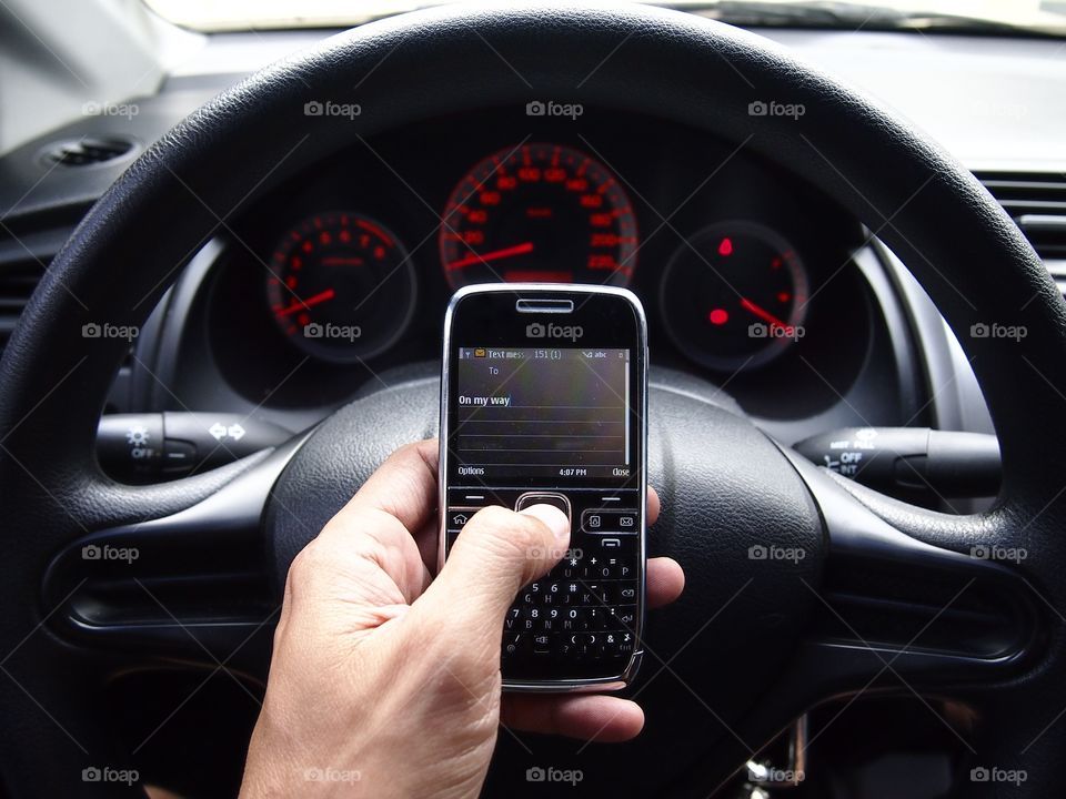 hand holding a cellphone in front of a car's steering wheel
