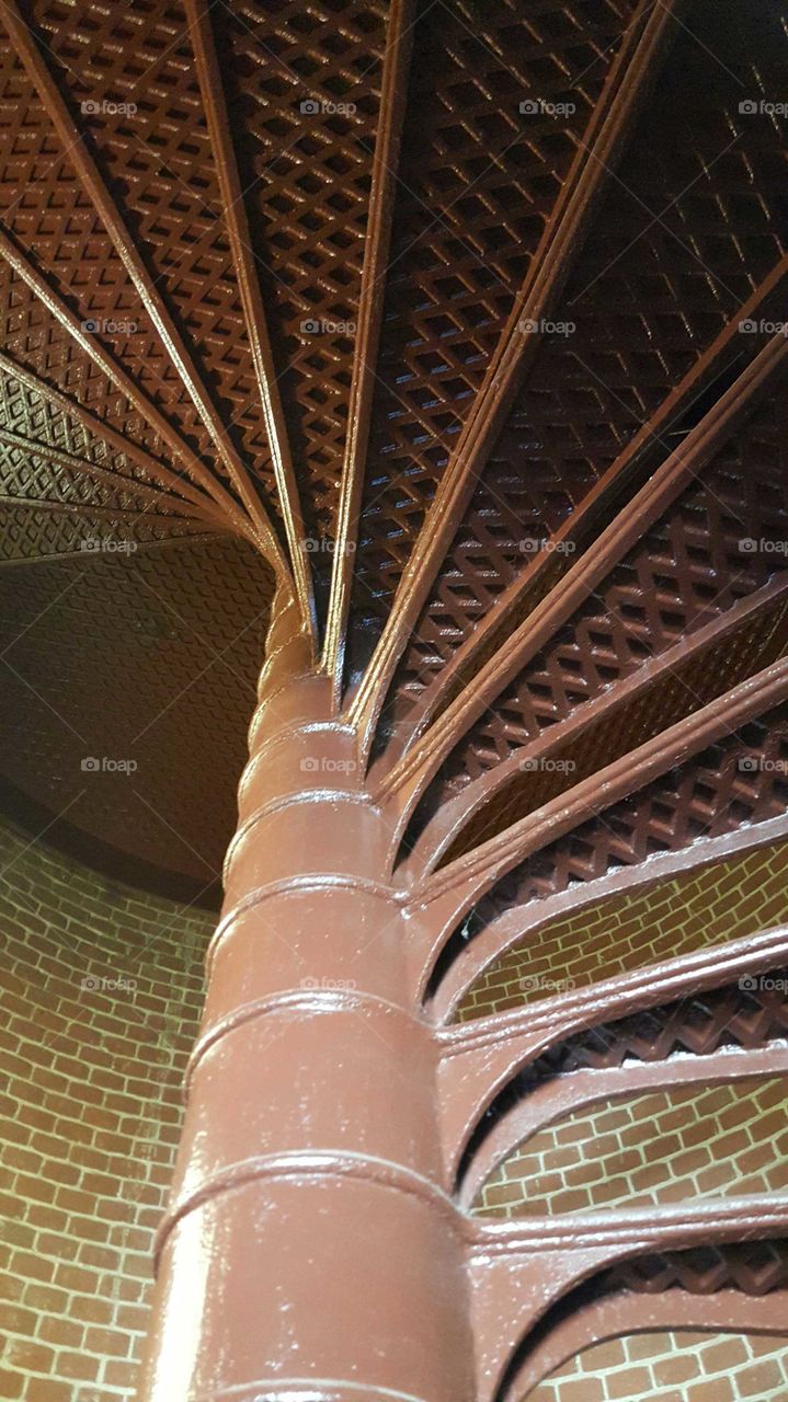 A spiral metal staircase in an old lighthouse twists upward step by step.