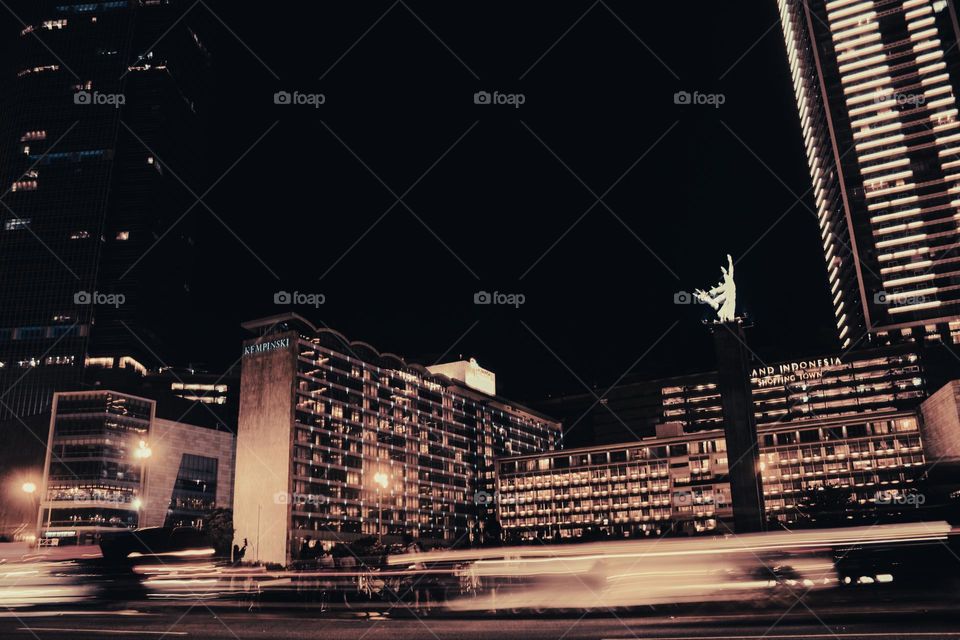 View of the Bunderan HI or Welcome Monument at night in downtown Jakarta with a Hotel and business center building in the background on Jalan Jenderal Sudirman, Jakarta, Indonesia.