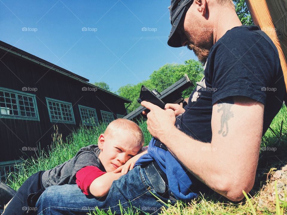 Father looking on his phone while his son resting in his lap