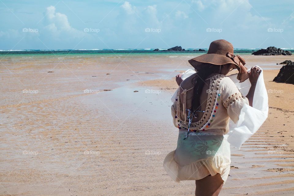 Girl walking in the hot sunny beach with hat