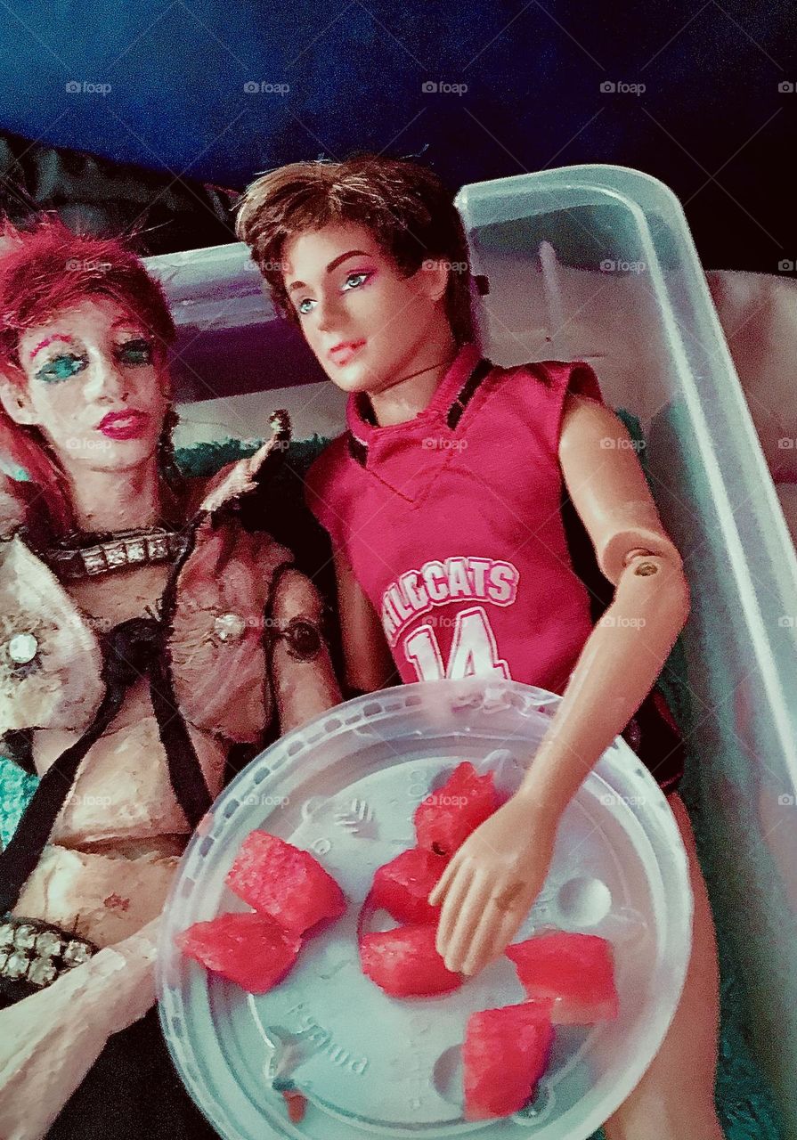 „Davey“, my unique creation, a handmade „Barbie“ sized doll in the likeness of „David Bowie“ approximately aboard the „Salvation“ enjoys a cool summertime treat of watermelon with his very good „Mattel“ made friend Michael. 2020. Hypnotic Productions