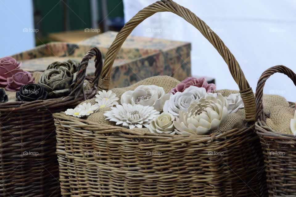 Ceramic flowers in a wooden basket for sale on the market. Closeup image showing the flowers.