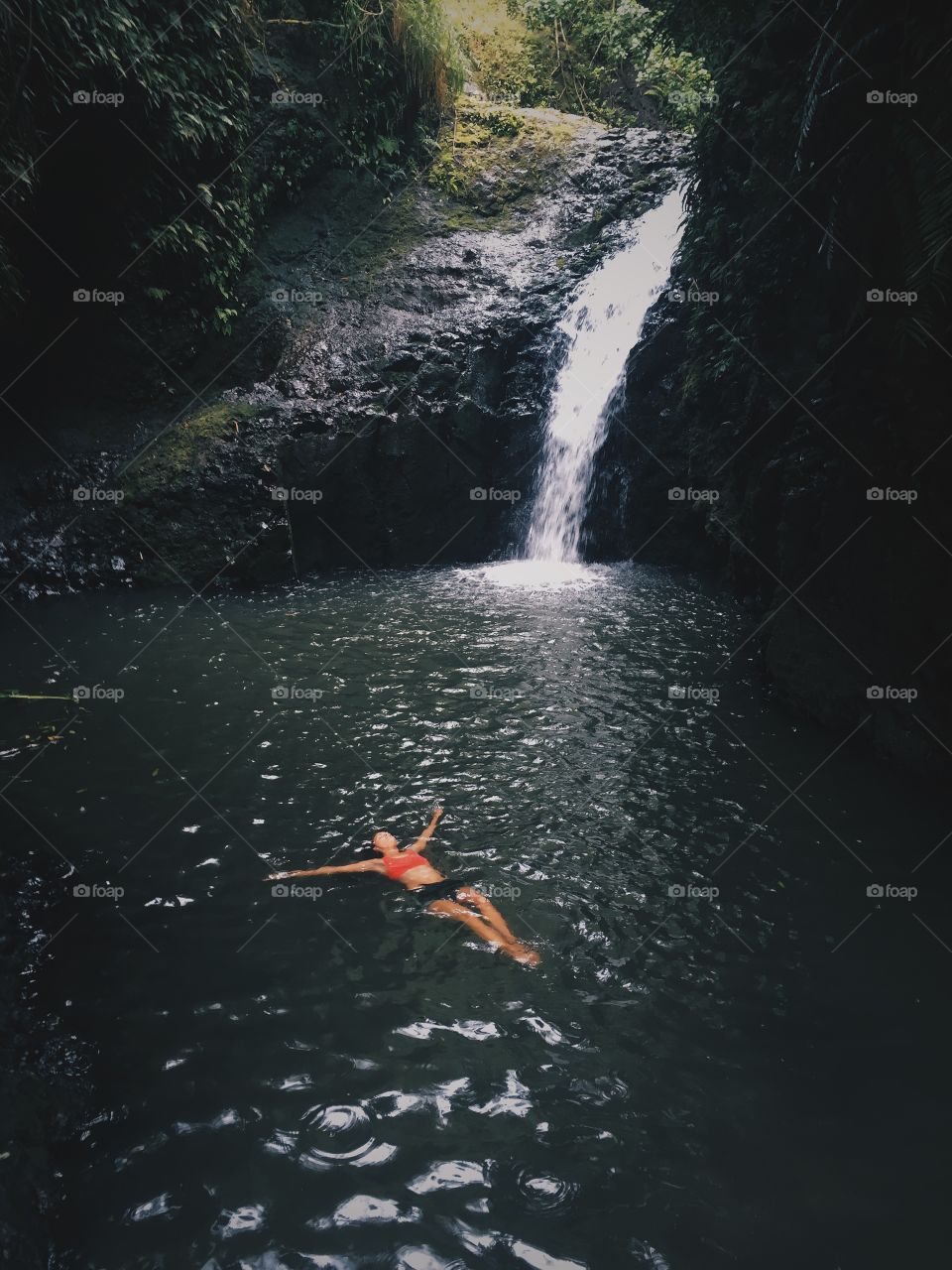 Girl relaxes in tropical waterfall in Hawaii.