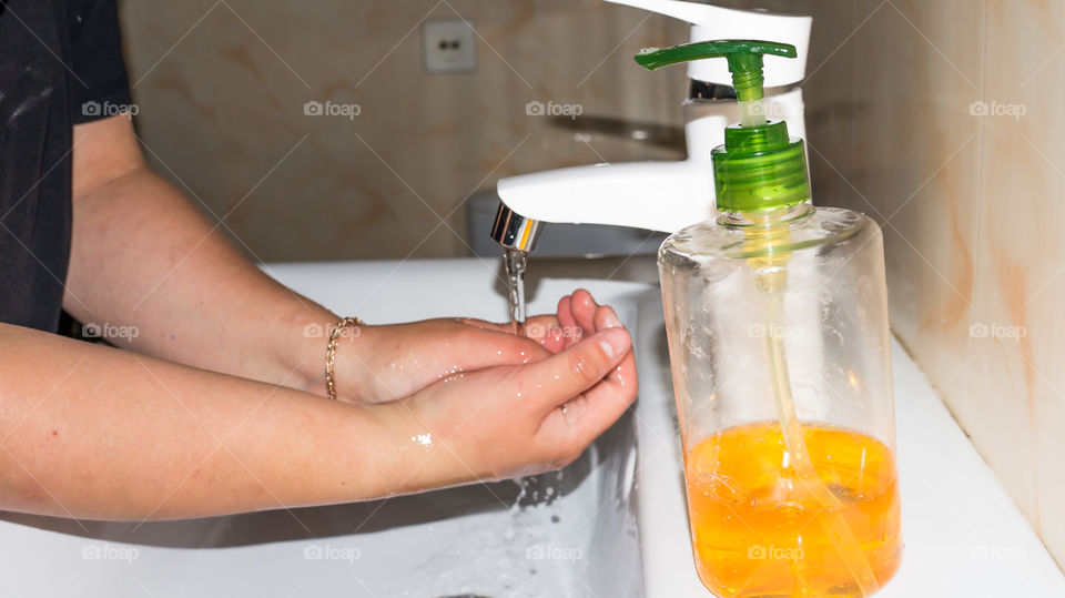 A man thoroughly washes his hands with soap in the bathroom, in a white washbasin with a white tap and antibacterial soap, makes a lot of foam and washes fingers and brushes after walking on the stree