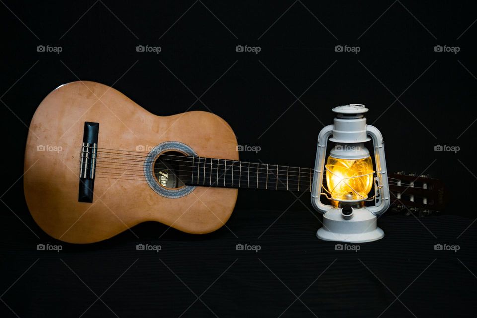 Wooden guitar next to a metal lamp, with a black background