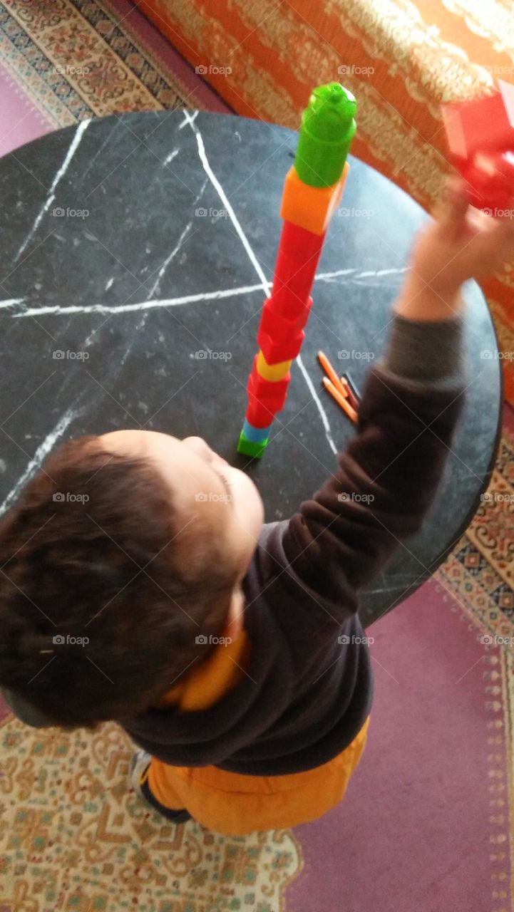 A little boy trying to make a building with toys..