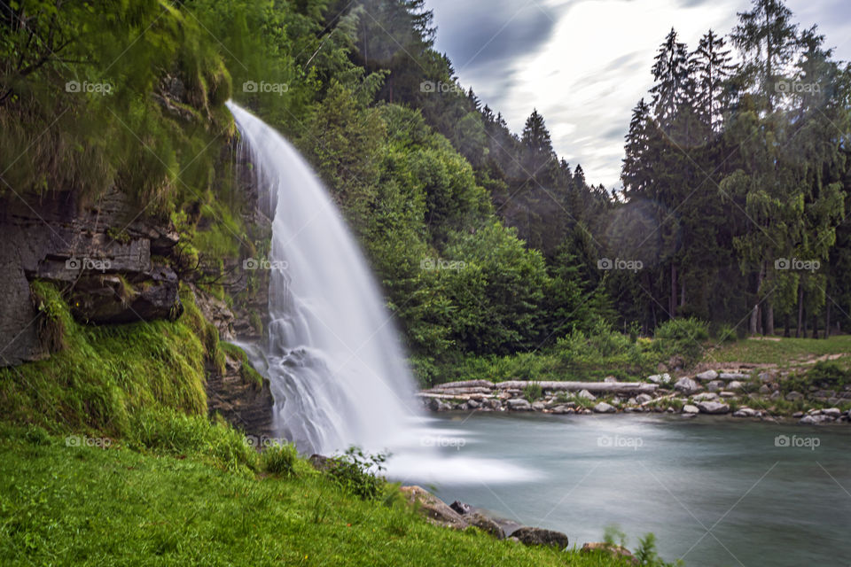 Long side exposure of the pretty Piumogna waterfall in Faido (CH) with its pond and the green forest that contains it. A romantic postcard of an idyllic alpine landscape.