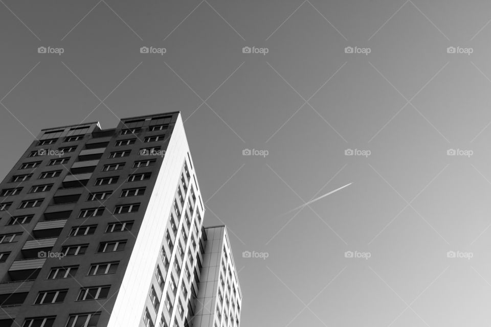 Fly away from city life. Airplane trail in sky with high rise apartment building, monochrome processing, travel concept