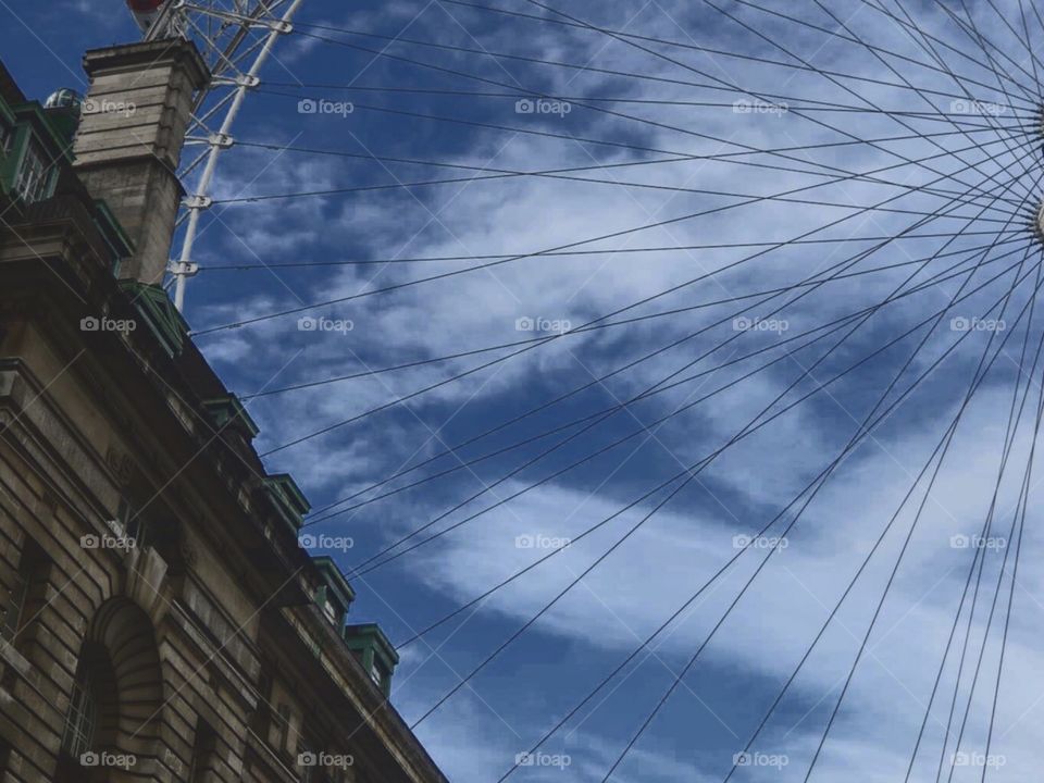 A quadrant of the London eye, obstructed by some great architecture. With a blue sky and cloud background 