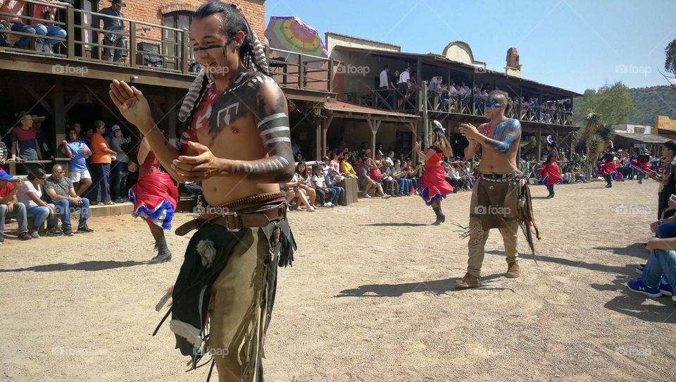 Women dressed with red skirts and men dancing on rustic street.