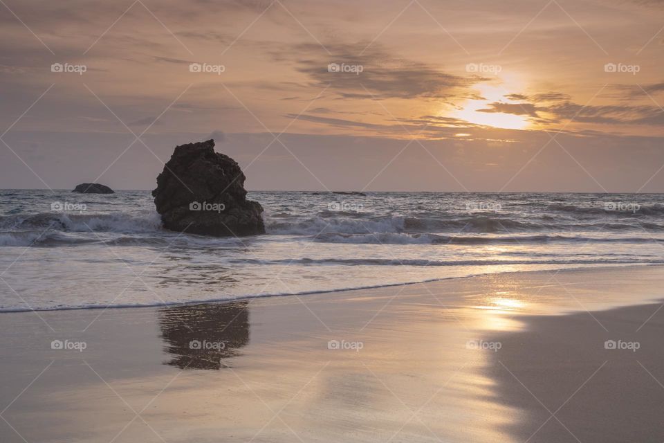 Beautiful sunset with reflection over the water. Isolated rock and reflection make dramatic scenery. Galle, sri lanka