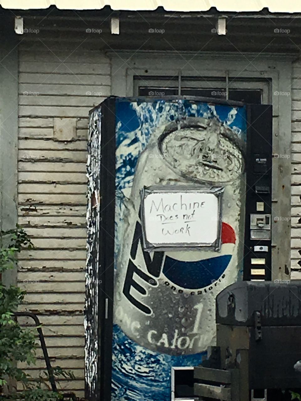 Broken down pop vending machine in an old front porch with a sign that says “Machine Does Not Work” on it.