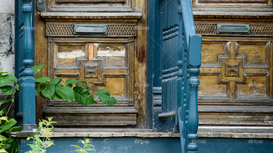 Freshly painted blue railings next to rustic old vintage wooden doors with ornate woodwork deteriorating and needing repair 