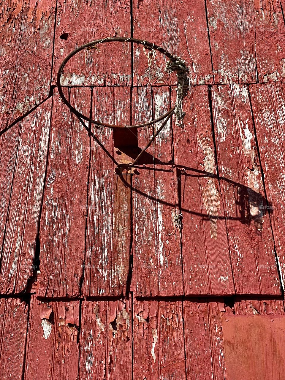 An old basketball hoop on the side of a red barn