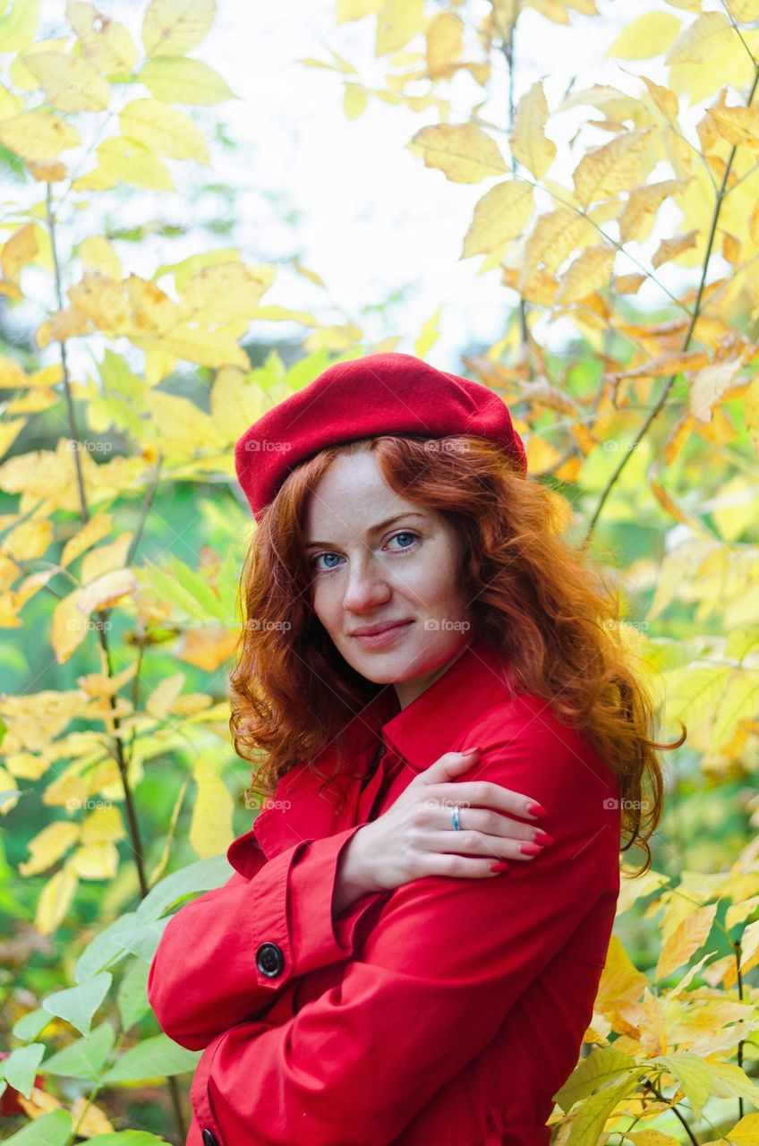 Portrait of beautiful young redhead curly woman in red beret and coat stands in autumn Park.  Happy lifestyle.