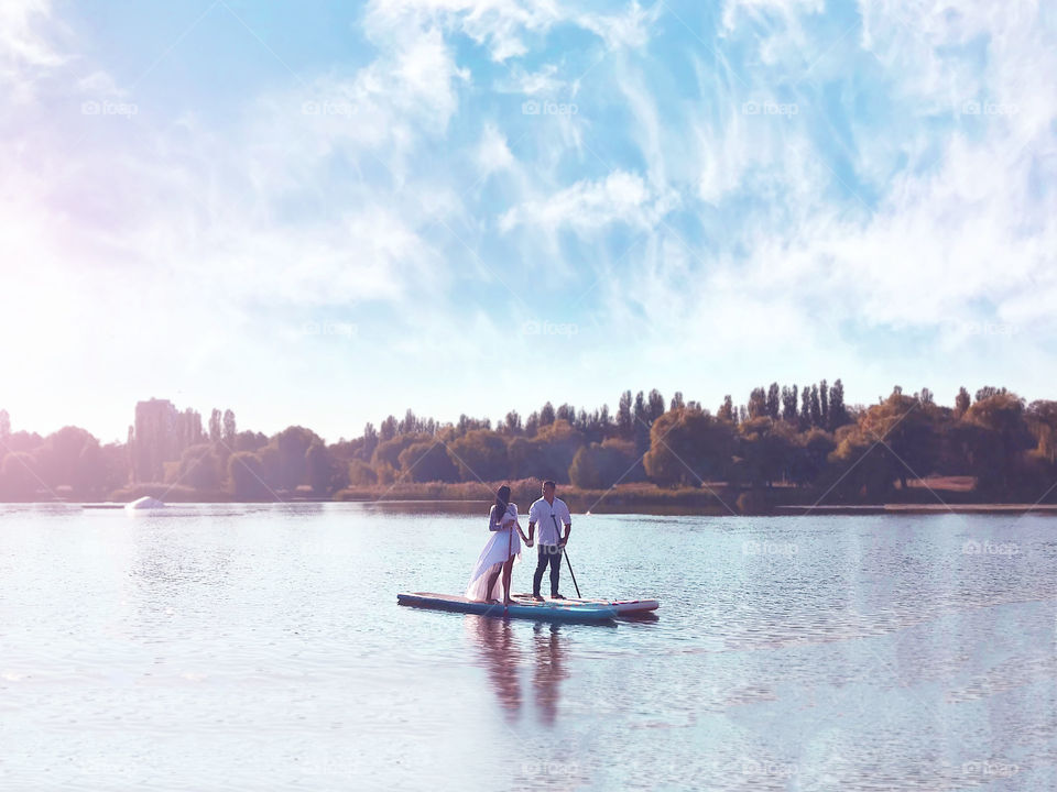 Couple in love holding hands and standing on the paddle boards in the middle of the lake with mist in front of autumn trees on the horizon 
